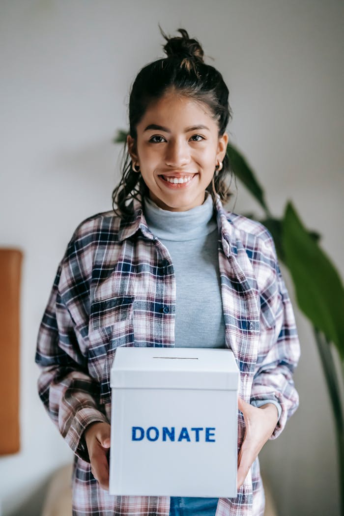 Cheerful woman holding a box labeled Donate indoors, symbolizing charity and kindness.